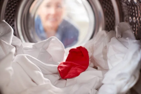 白い洗濯物と混ぜた赤い靴下で洗濯機の中を見ている女性 — ストック写真