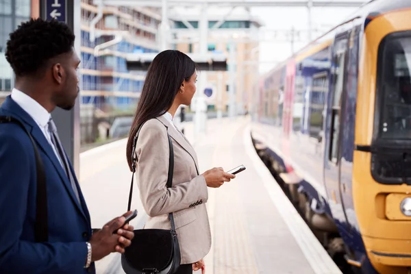 電車を待つ鉄道のプラットホームで通勤するビジネスマンとビジネスウーマン — ストック写真