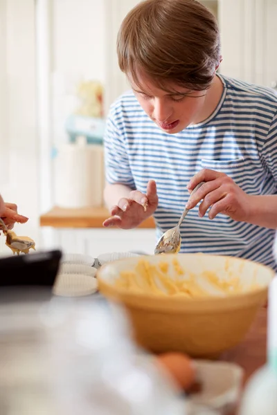 若いダウンズ症候群の男性は 自宅でキッチンでカップケーキを焼く — ストック写真
