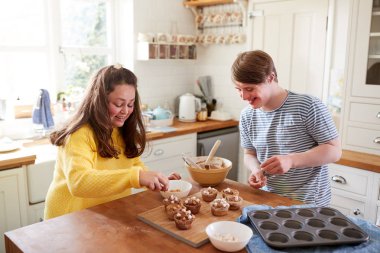Young Downs Syndrome Couple Decorating Homemade Cupcakes With Marshmallows In Kitchen At Home clipart