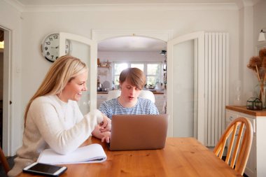 Downs Syndrome Man Sitting With Home Tutor Using Laptop For Lesson At Home clipart
