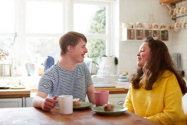 Young Downs Syndrome Couple Enjoying Tea And Cake In Kitchen At Home