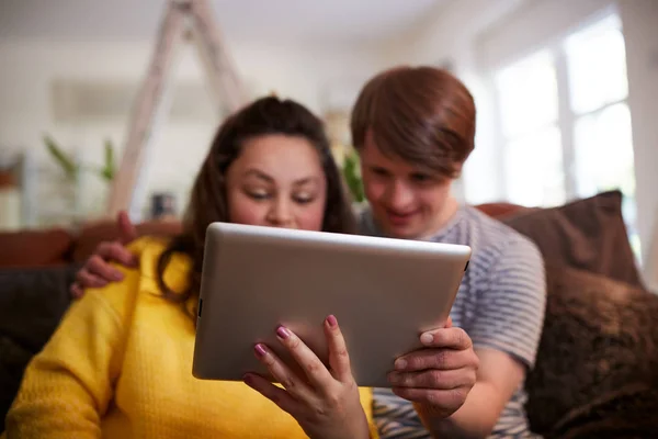 自宅でデジタルタブレットを使用してソファに座っている若いダウン症候群のカップル — ストック写真