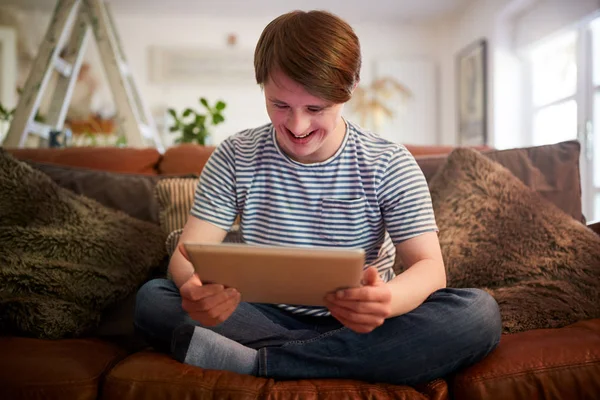 Homem Jovem Síndrome Downs Sentado Sofá Usando Comprimido Digital Casa — Fotografia de Stock
