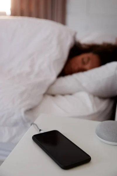 ベッドサイド テーブルの上の携帯電話が付いているベッドで眠っている女性 — ストック写真
