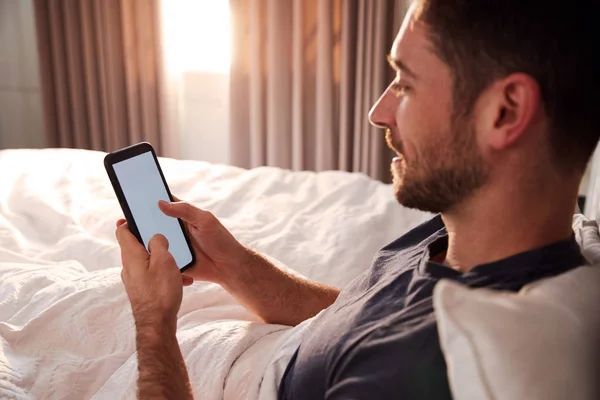 醒来后 男人坐在床上看着手机 — 图库照片