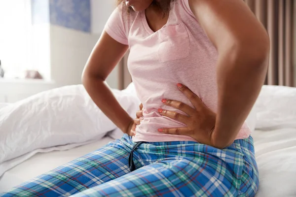 自宅のベッドに座って期間の痛みに苦しむパジャマを着た女性のクローズアップ — ストック写真