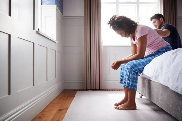 自宅のベッドに座ってうつ病に苦しむパジャマを着た男性慰め女性 — ストック写真