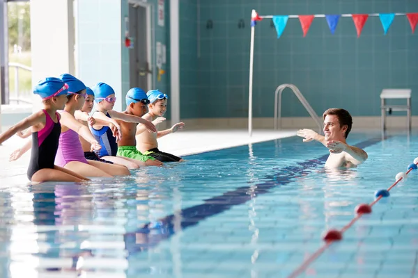 물에서 코치는 그들이 수영장의 가장자리에 앉아으로 수업에서 아이들에게 지침을 제공합니다 — 스톡 사진