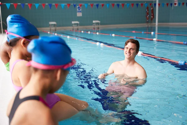 男教练在水中给孩子在游泳课上的指示 因为他们坐在池边 — 图库照片