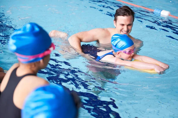 Male Coach In Water Giving Group Of Children Swimming Lesson In Indoor Pool