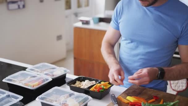 フィットネスウェアを身に着けている男は自宅でキッチンで健康的な食事のバッチを準備 スローモーションで撮影 — ストック動画