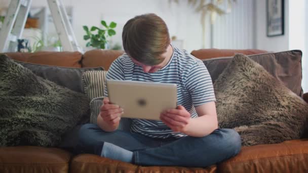 Young Downs Syndrome Hombre Sentado Sofá Viendo Transmisión Películas Tableta — Vídeos de Stock