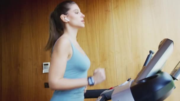在家里跑步机上跑步的女人穿着无线耳机在智能手表上检查健身应用程序的特写镜头 慢动作 — 图库视频影像