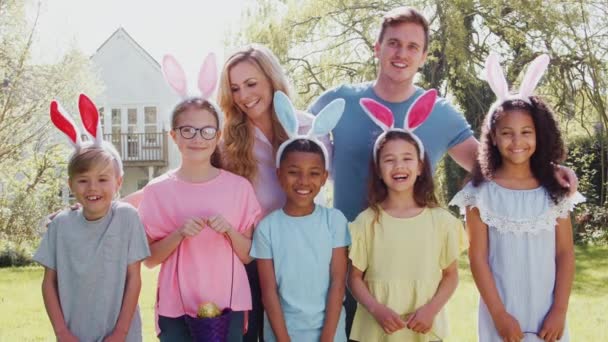 一组穿着兔子耳朵的父母和孩子们在花园里打猎复活节彩蛋的画像 他们在镜头前微笑着 动作缓慢 — 图库视频影像