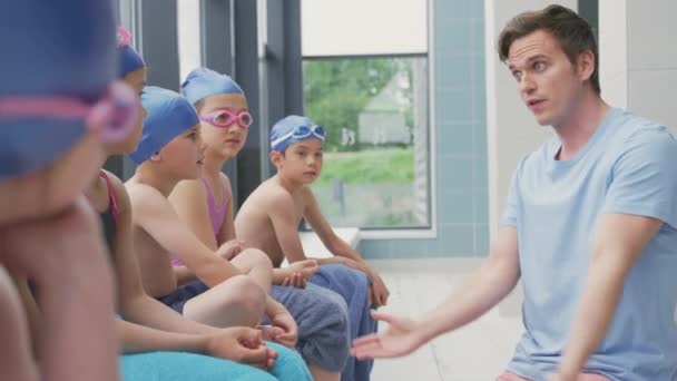 水泳プールに座っている子供たちのグループは 男性コーチによる説明を与えられています スローモーションで撮影 — ストック動画