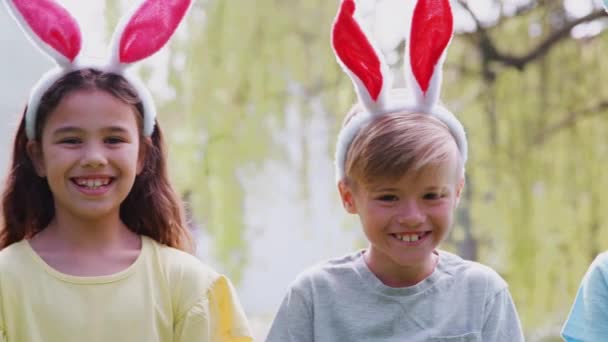 カメラで笑顔の庭でイースターエッグハントにウサギの耳を身に着けている子供たちのグループの肖像 スローモーションで撮影 — ストック動画
