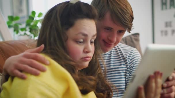 Młoda Para Zespołem Downa Siedząca Kanapie Oglądająca Film Strumieniowo Tabletu — Wideo stockowe