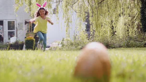 若いです女の子オンイースターの卵狩り実行している庭を渡ってとピックアップチョコレートの卵に入れバスケット スローモーションで撮影 — ストック動画