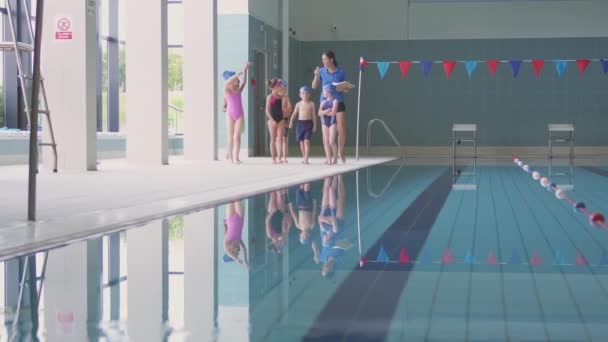 女教练在游泳课上带着孩子们沿着游泳池边慢慢走向摄像镜头 — 图库视频影像