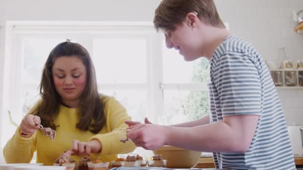 年轻的唐斯综合症夫妇在家里的厨房里烘焙 用慢动作的冰球装饰纸杯蛋糕 — 图库视频影像