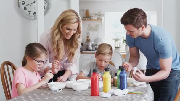 家族は子供たちがイースターのために卵を描くのを助ける両親とキッチンテーブルの周りに座っています スローモーションで撮影 — ストック動画