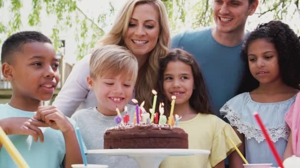 両親や友人と庭で屋外パーティーを楽しんで誕生日を祝う男の子はケーキの上にろうそくを吹きます スローモーションで撮影 — ストック動画