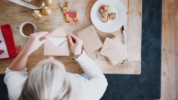 頭上からの眺めテーブルに座っている女性を見下ろすクリスマスカードを書きながらクッキーを食べる — ストック動画