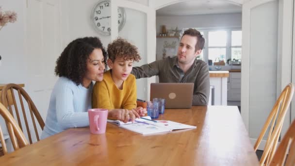 当父亲在笔记本电脑上工作时 母亲和儿子一起坐在桌旁帮助做家庭作业 动作缓慢 — 图库视频影像