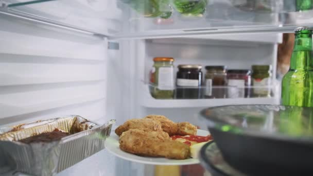 从冰箱里往外看 女人打开门 拿出一盘不健康的剩菜 外卖炸鸡和披萨 动作缓慢 — 图库视频影像