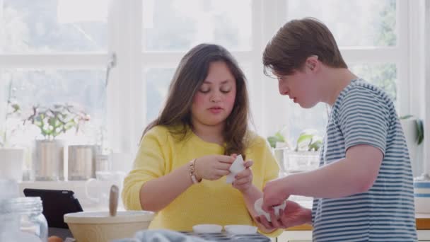 年轻的唐氏综合症夫妇在家厨房里烘烤着 慢动作地把纸杯蛋糕盒放进盘子里 — 图库视频影像
