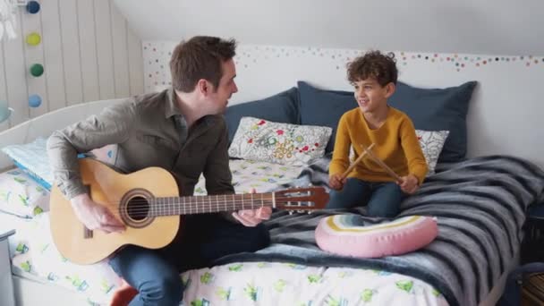单身父亲在家里的卧室里和儿子一起弹着吉他 他在地板垫子上打鼓 动作缓慢 — 图库视频影像