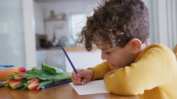 Junge Sitzt Mit Blumenstrauß Tisch Und Schreibt Muttertagskarte Aufgenommen Zeitlupe — Stockvideo