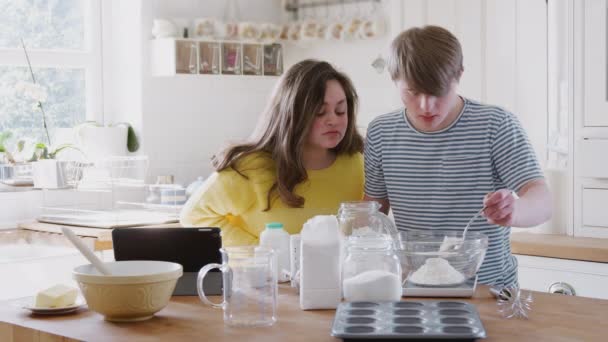 若いダウン症候群のカップルは デジタルタブレット上のレシピと一緒にケーキを焼くために成分を測定した後 自宅でキッチンで スローモーションで撮影 — ストック動画