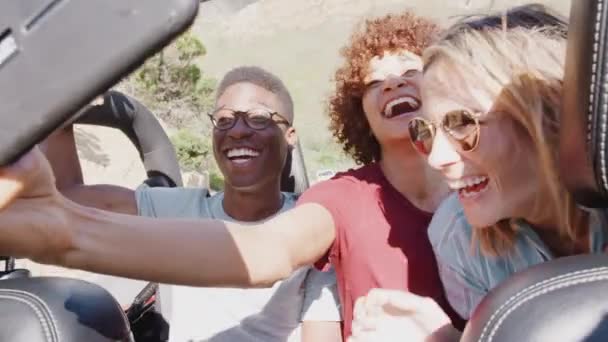 一群坐在敞篷轿车后面的年轻朋友们在暑假开车沿着乡间小路开车时 用手机自拍 慢镜头拍摄 — 图库视频影像