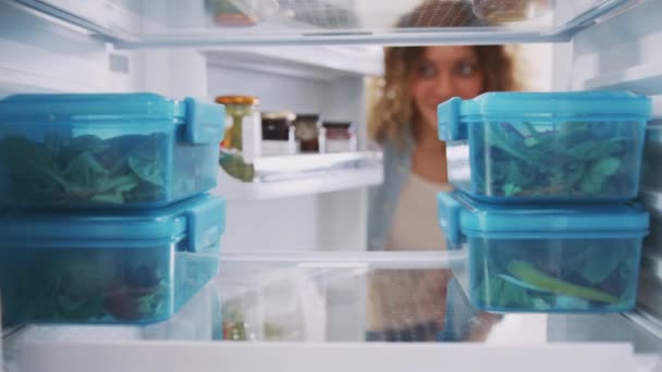 女性がドアを開けて プラスチック容器で調理済みの食事を取るように冷蔵庫の中から見る スローモーションで撮影 — ストック動画