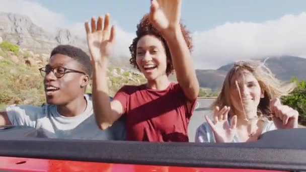 興奮した若い友人のグループは 夏休みに国の道路に沿ってオープントップカーの運転の後ろに立ち上がる スローモーションで撮影 — ストック動画
