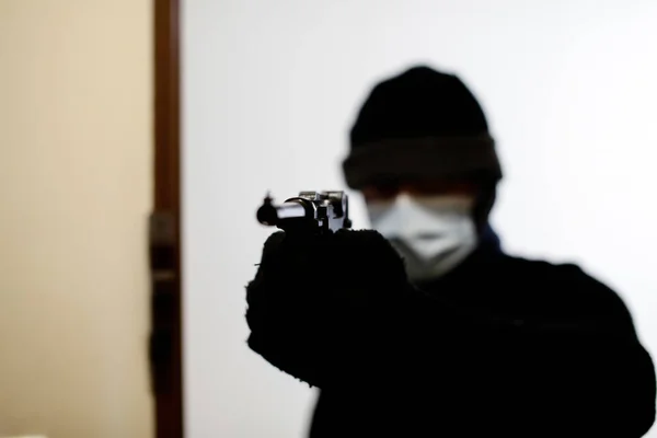 A burglar breaking into a house, pointing a gun and wearing a face mask. Silhouette of a man with a gun.