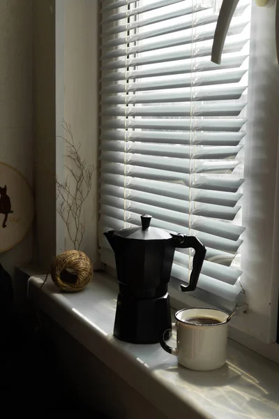 Coffee maker with a cup of freshly brewed coffee on a windowsill in the morning at sunrise