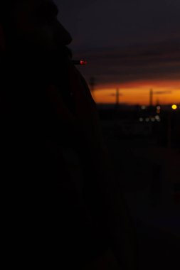 Gökyüzü gün batımında, sakallı bir adamın arka planında sigara içen kulelerle dolu. Yüksek kalite fotoğraf