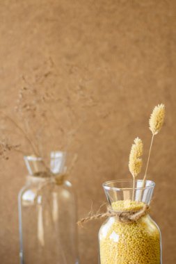 Millet cam kavanozun içinde ahşap bir standın üzerinde, sonra bir buğday kulağı, bej bir arka planda