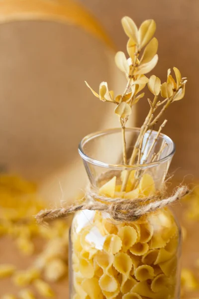 Pasta in a jar, a lot of pasta is scattered around, a jar stands on a wooden stand. High quality photo