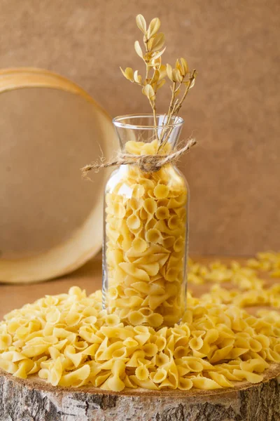 Pasta in a jar, a lot of pasta is scattered around, a jar stands on a wooden stand. High quality photo