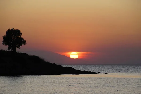    Denizüzerinde kızıl gün batımı. Yunanistan'da Eylül. Sithonia. Güneş, bulutlar ve sıra dışı renkler. Suda parıldama. Güneş ufukta yokuş aşağı gidiyor                            