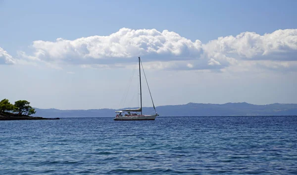 Holidays at sea. Pleasure yacht on the horizon. September in Greece. Sithonia. Blue sea and white clouds