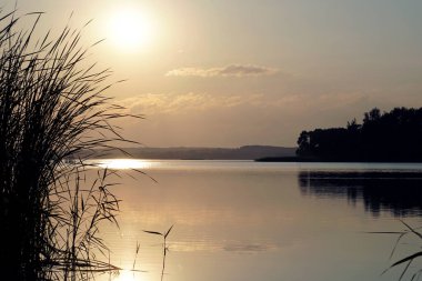  Gölün üzerinde sakin, sıcak bir yaz akşamı. Güneş ve bulutlar. Gün batımı. Yatay manzara                              
