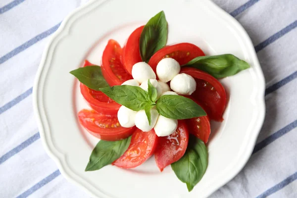Domates Mozzarella peyniri ve fesleğen yaprak beyaz bir plaka üzerinde