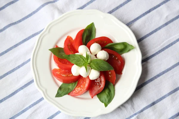 Domates Mozzarella peyniri ve fesleğen yaprak beyaz bir plaka üzerinde