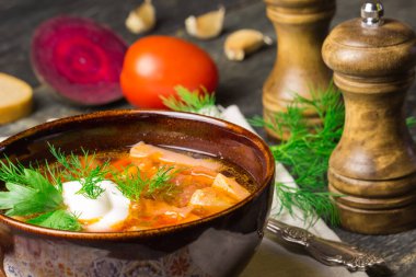 Borshch olan bir ev yapımı Rus, Ukrayna Ulusal çorba - kırmızı pancar, sebze ve et peçete, kaşık, domates, sarımsak ile Pancar çorbası gri bir ahşap zemin üzerine ekşi krema ile. Kırmızı plaka üzerinde