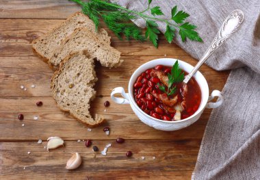 kırmızı fasulye çorbası beyaz kase, vintage kaşık, baharatlı otlar, Füme pastırma ile tahıl ekmek bir ahşap masa, rustik tarzı, üstten görünüm